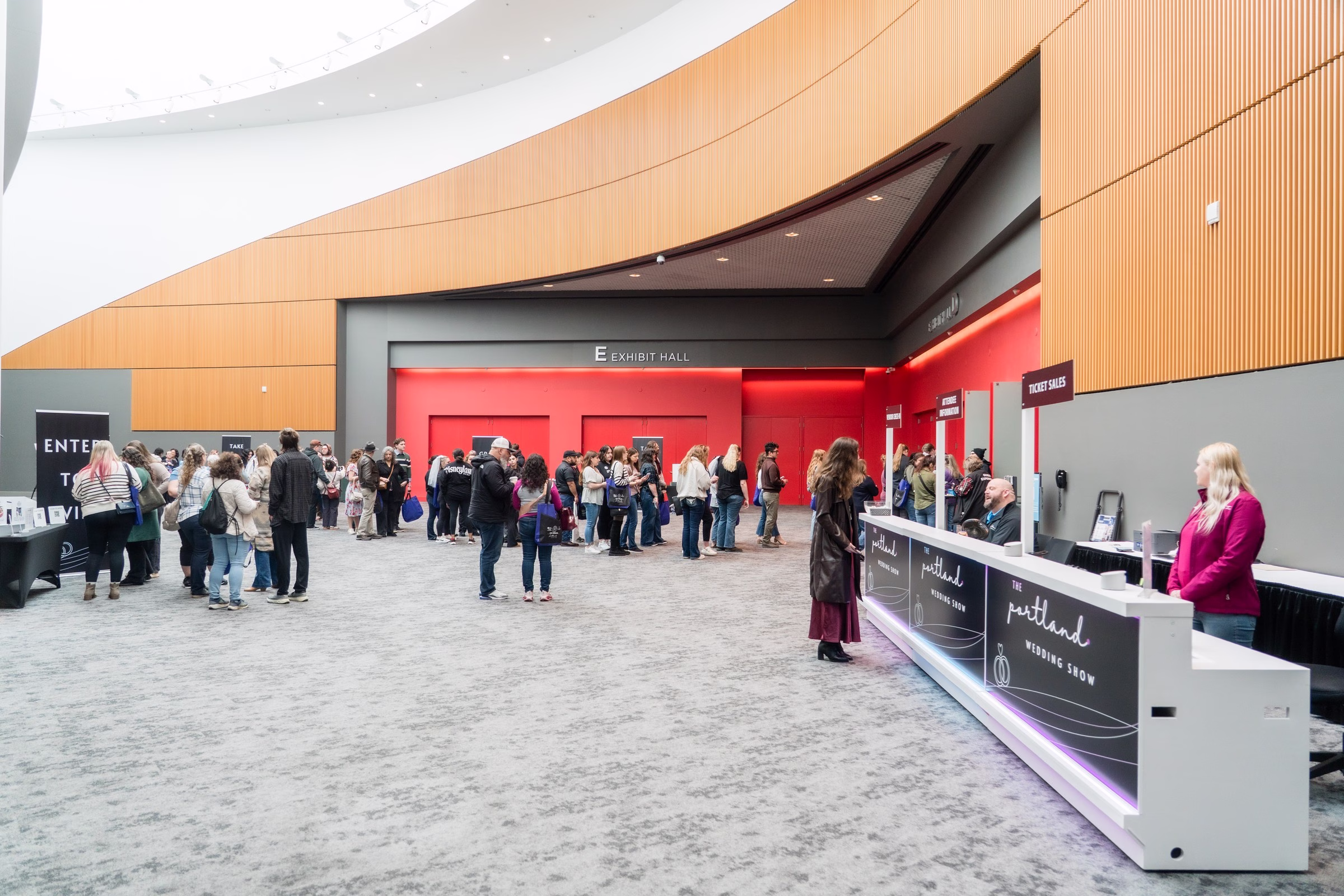 Portland Wedding Show 2024 exhibit hall entrance with attendees gathering near ticket sales counter and red exhibition space