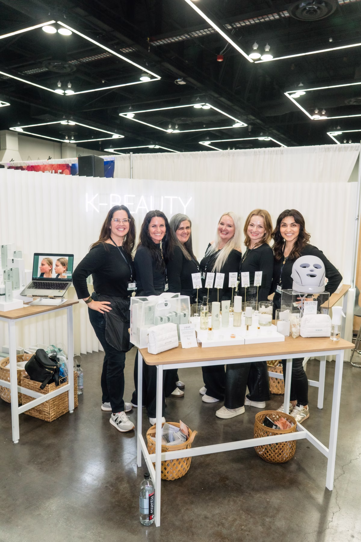 Beauty and skincare vendor booth with six female staff members displaying white product bottles and LED mask at Portland Wedding Show 2026