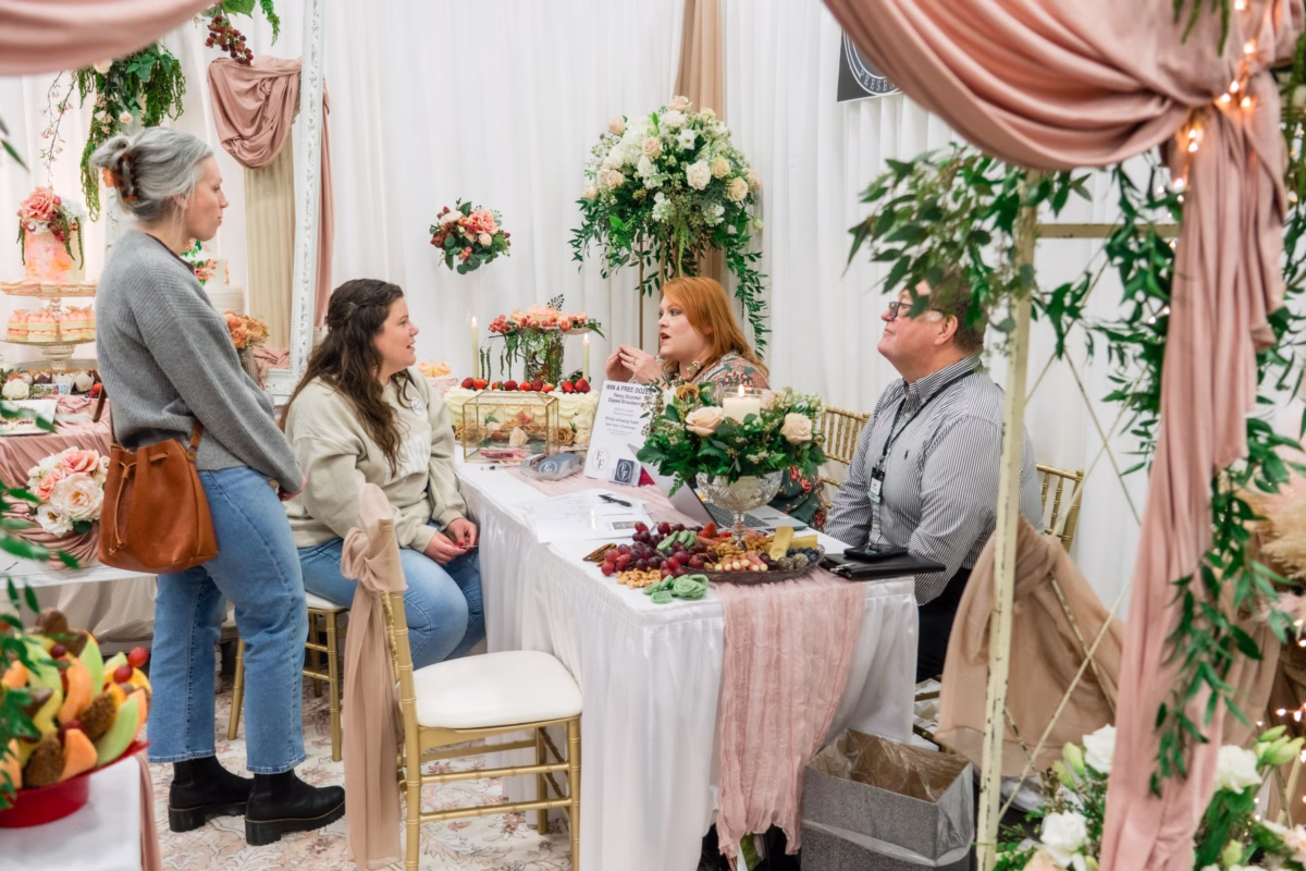 Wedding vendors consulting with engaged couples at decorated booth during Portland Wedding Show 2026 bridal expo