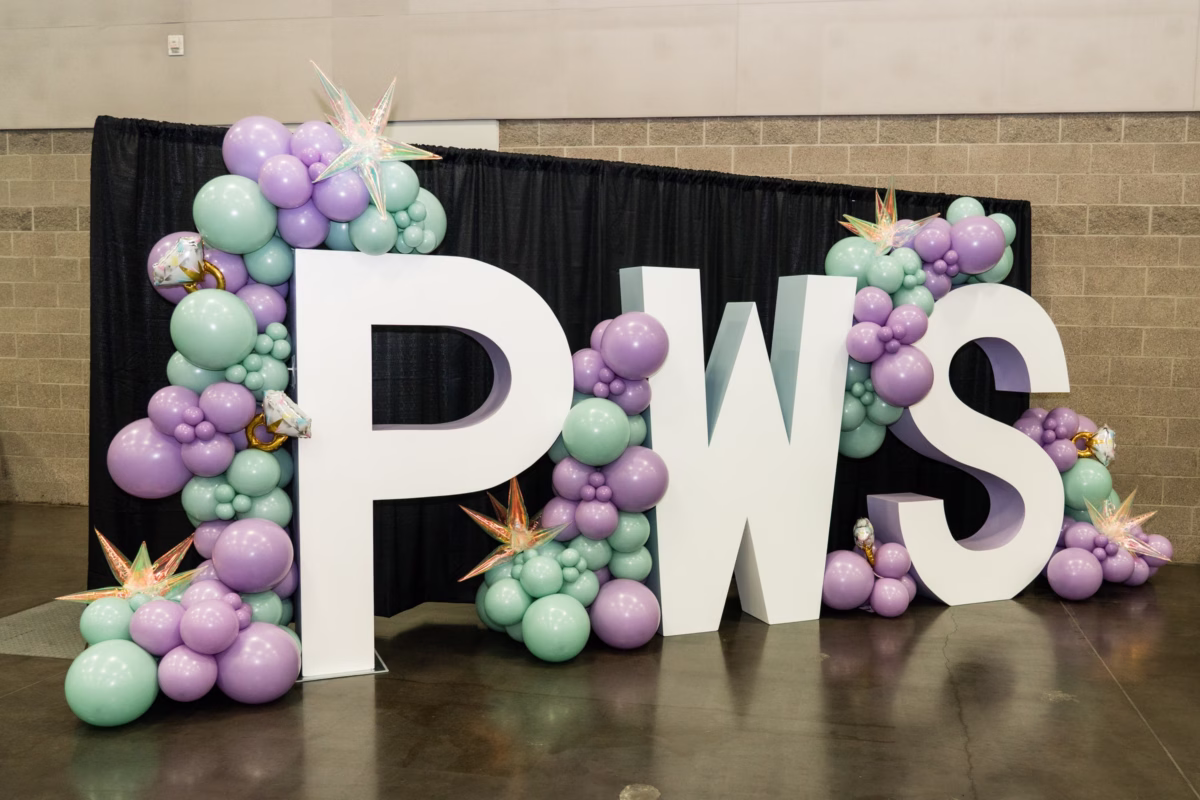 Large white PWS letters surrounded by purple and mint green balloon arrangements at Portland Wedding Show 2026 bridal expo